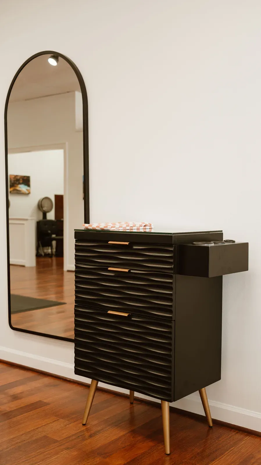 A black arched mirror over a black station with brass pulls