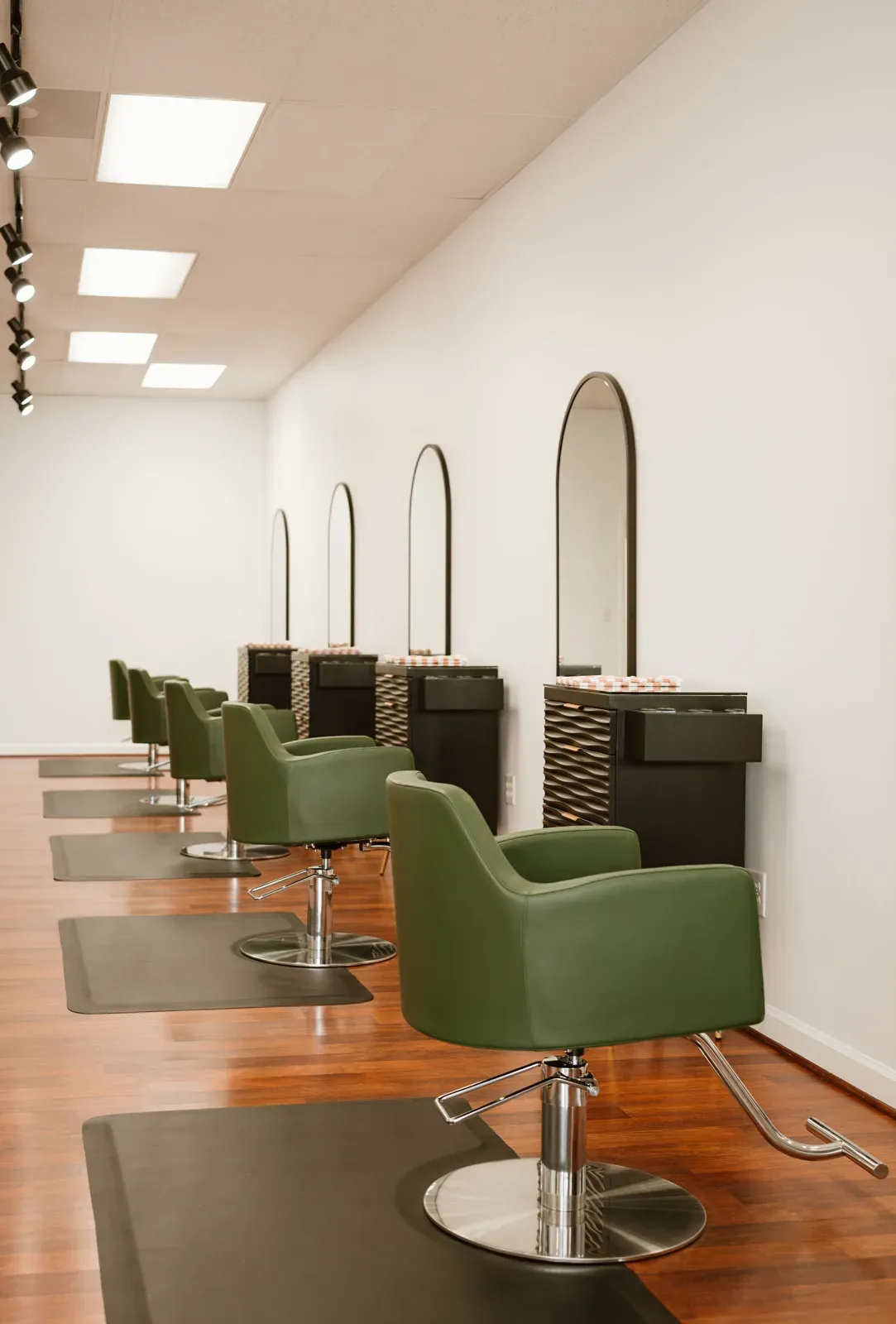 A row of spruce-green chairs at black arched mirrors