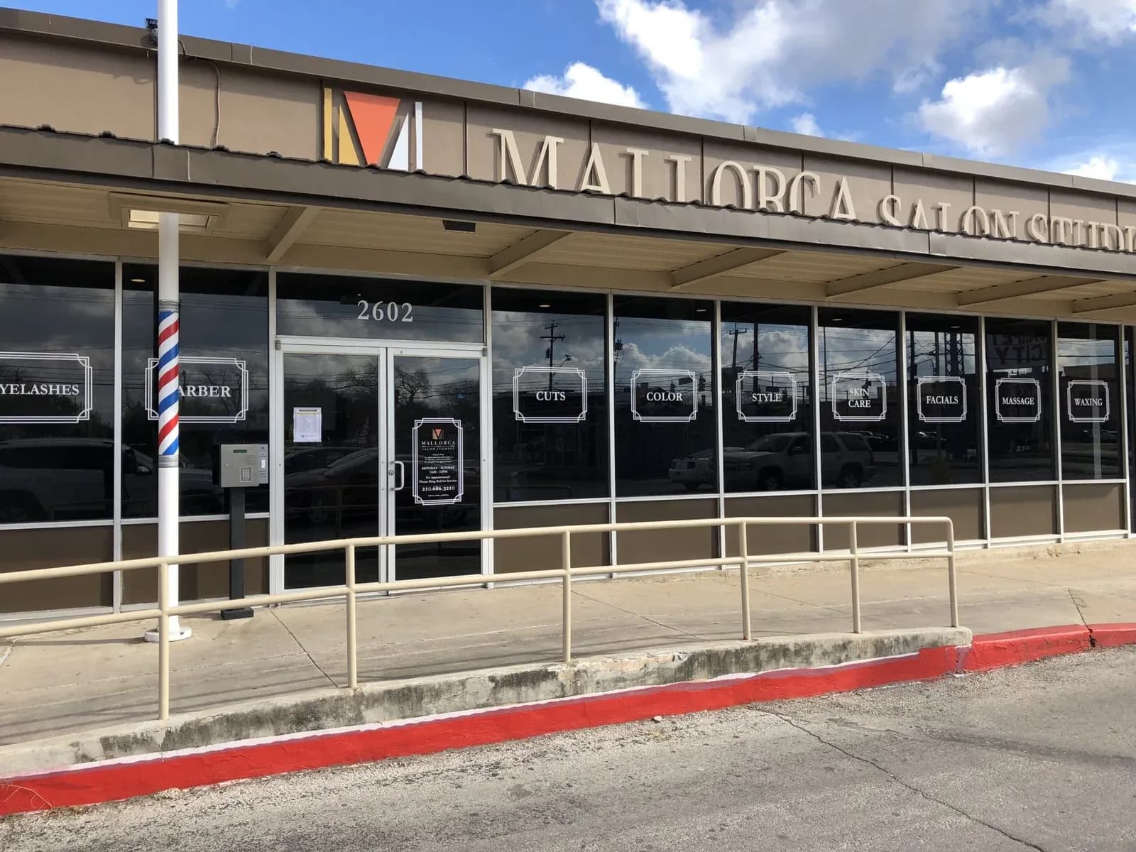 A Mallorca Salon Studios building with its sign and red curb